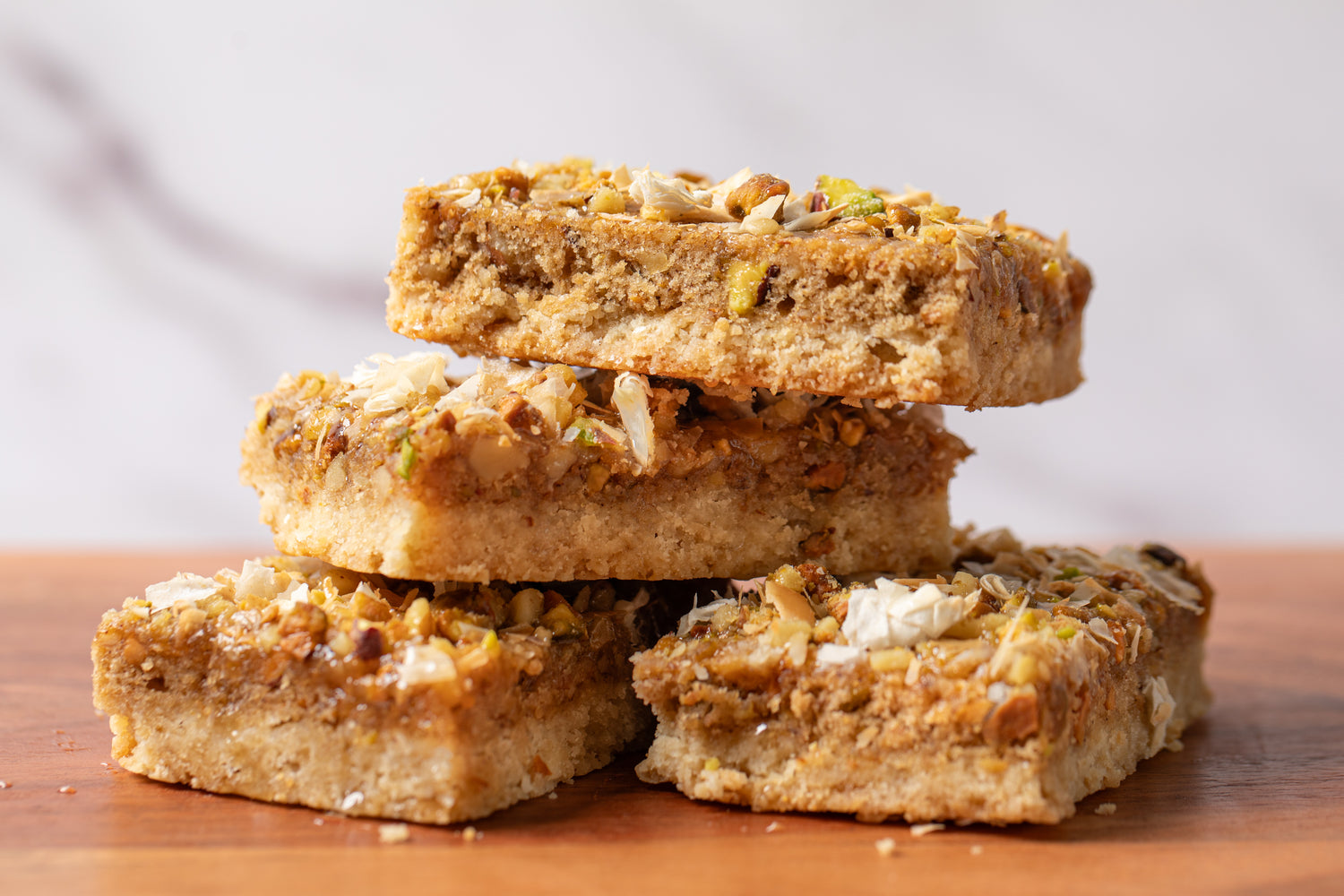 Indulgent dessert bar featuring a buttery shortbread base, topped with a blend of walnuts, pistachios, and delicate phyllo dough, capturing the rich flavors of baklava in every bite
