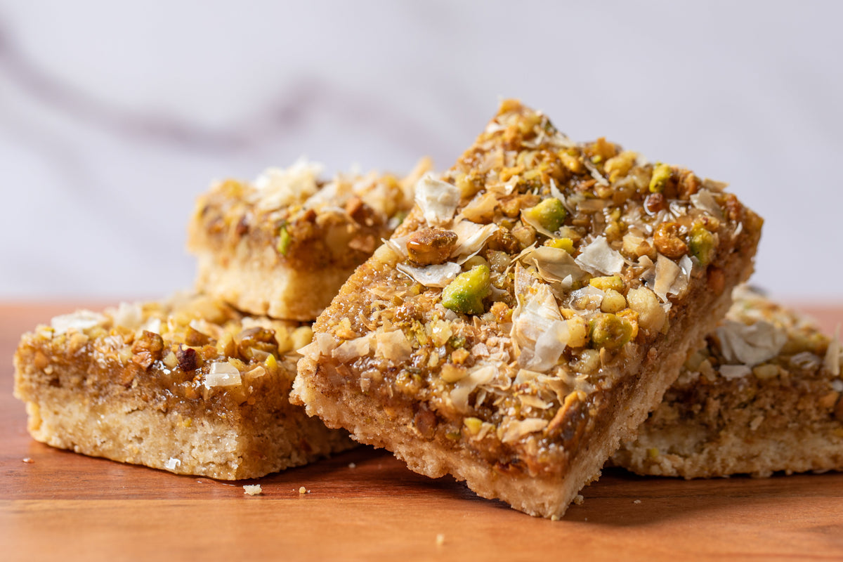 Delicious dessert bar with a rich shortbread crust, topped with a blend of walnuts, pistachios, and crispy phyllo dough, offering a perfect fusion of flavors inspired by traditional baklava