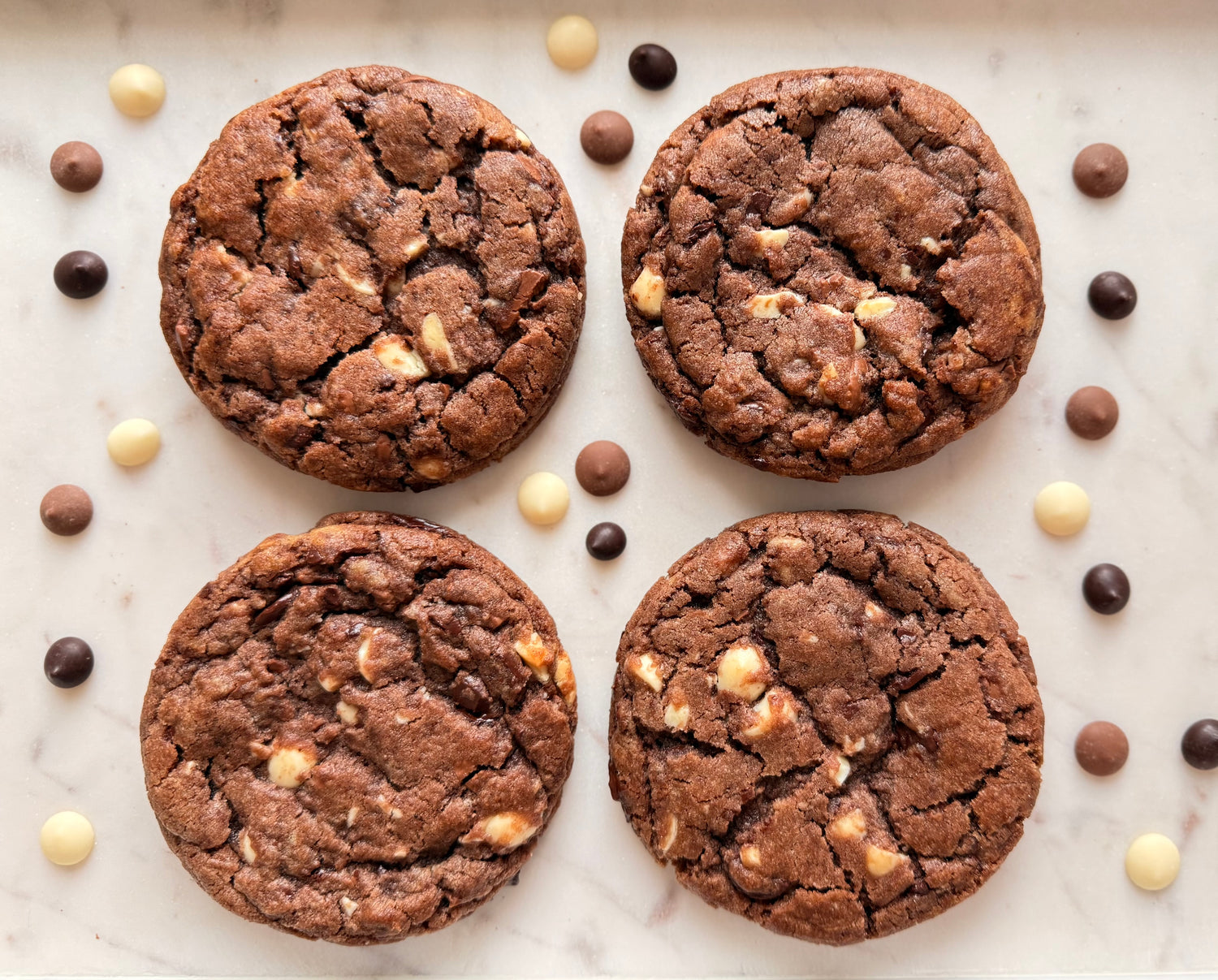 Four chocolate cookies with chocolate chips on a marble surface