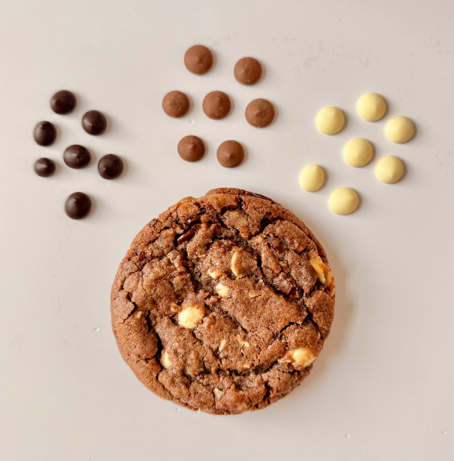 Chocolate cookie with dark, milk and white chocolate chips on a light background