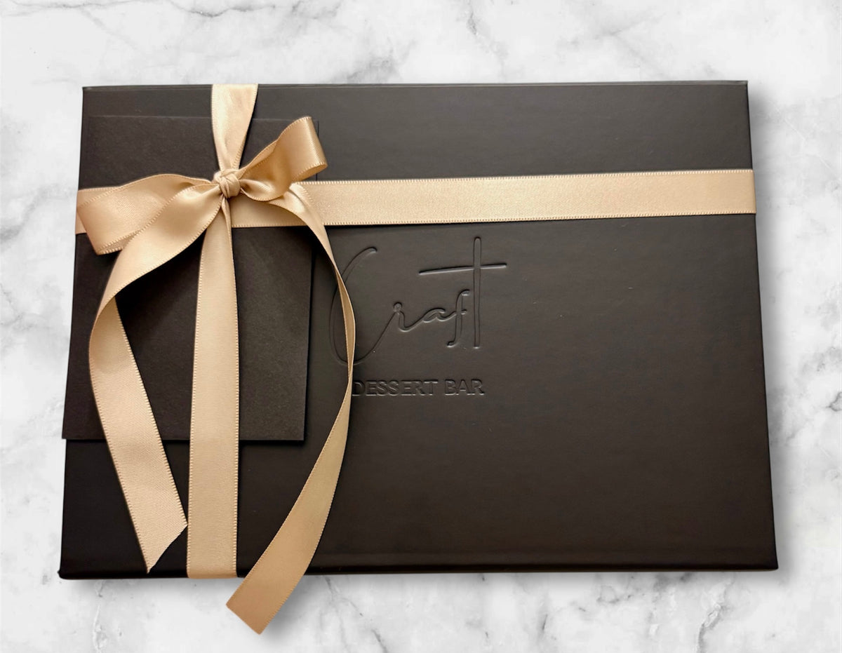 Luxury black gift box with gold ribbon and logo on a marble surface